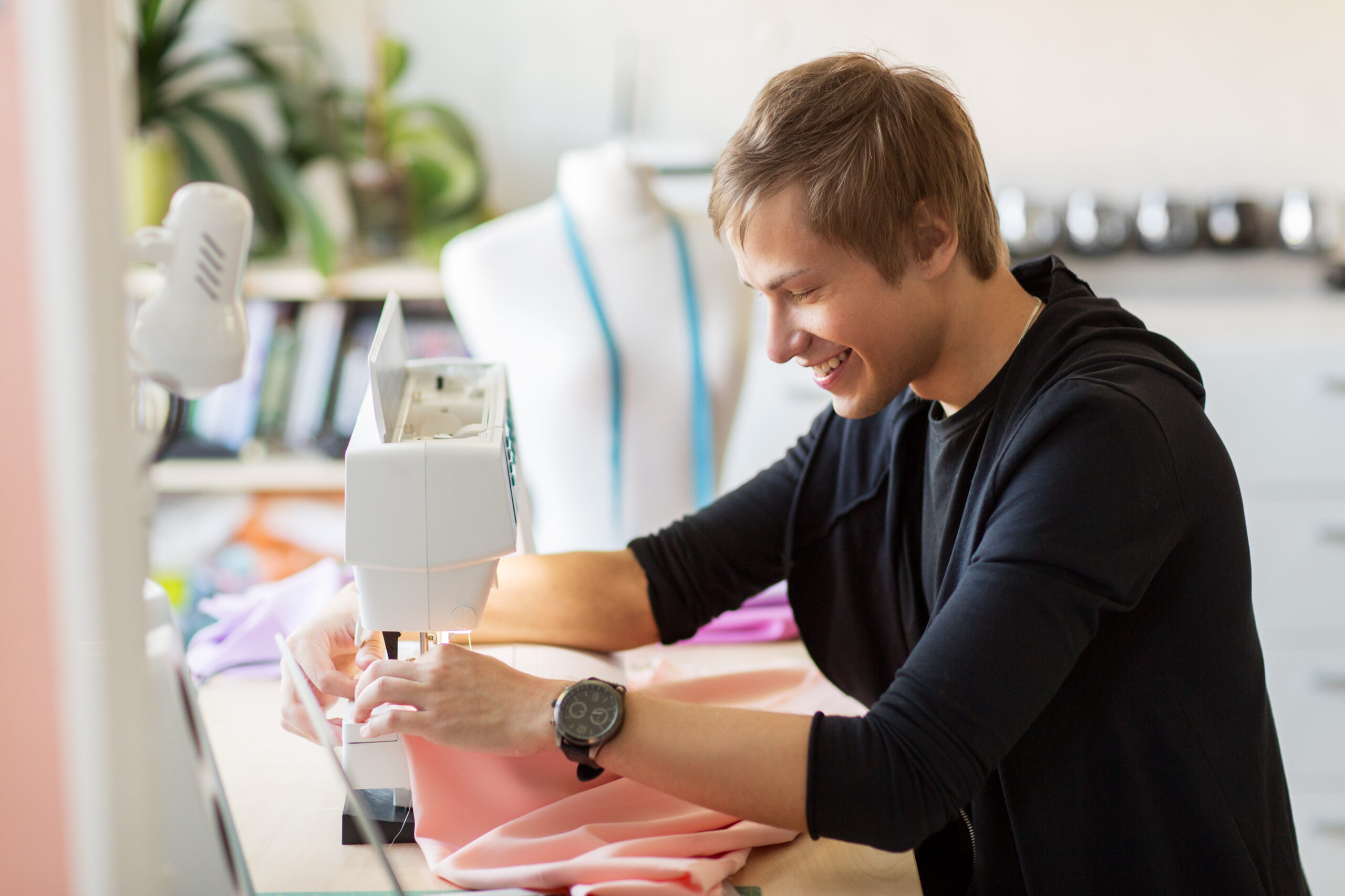 people, clothing and tailoring concept - fashion designer with sewing machine and cloth making new dress at studio