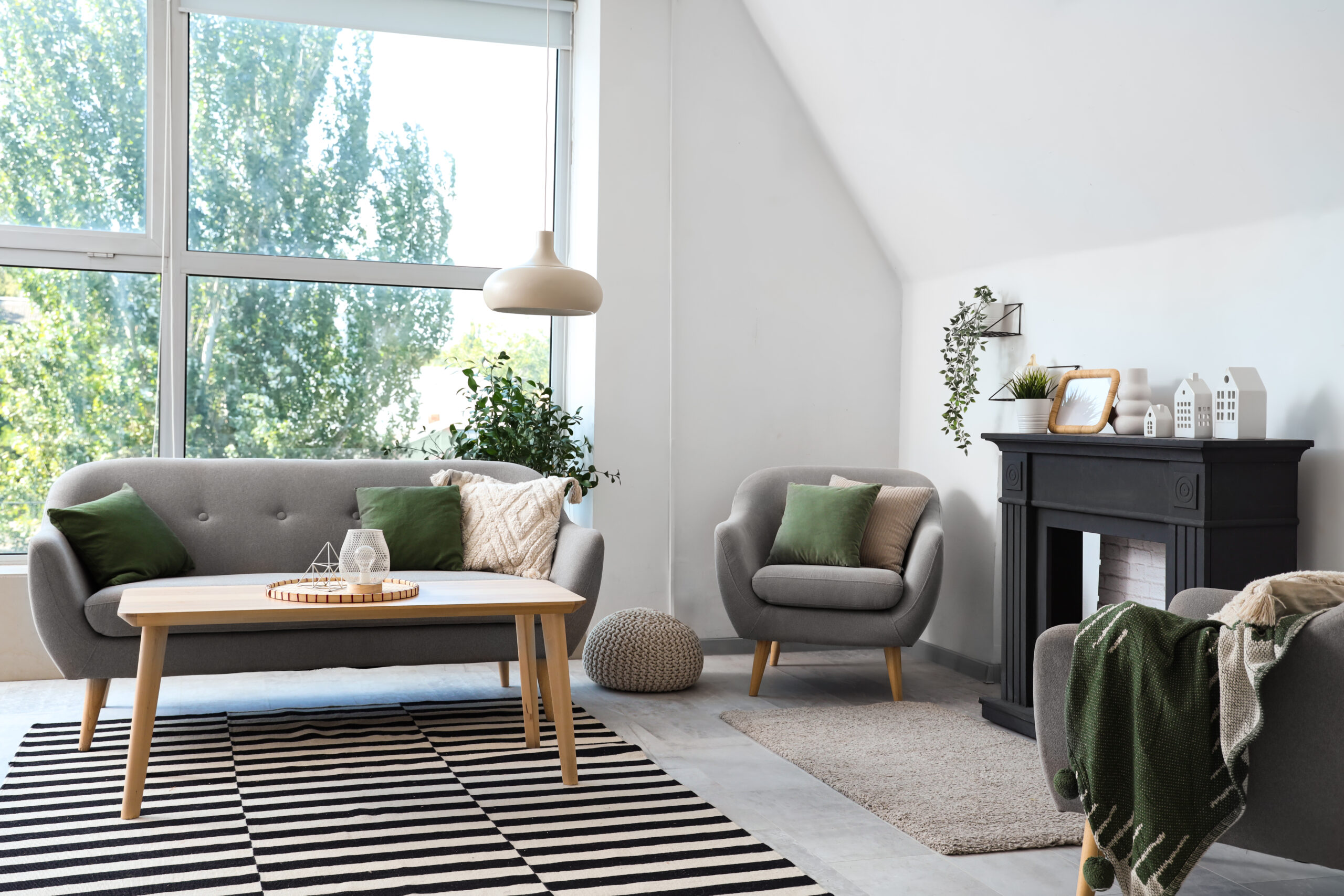 Interior of light living room with decorative fireplace, sofa and houseplants